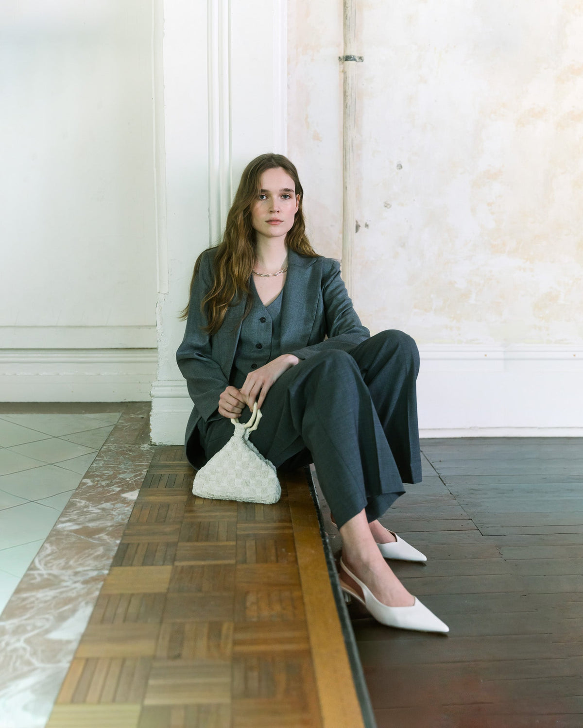 Model wearing charcoal tailoring holding an ivory beaded handbag with sculptural handle by The Hold.