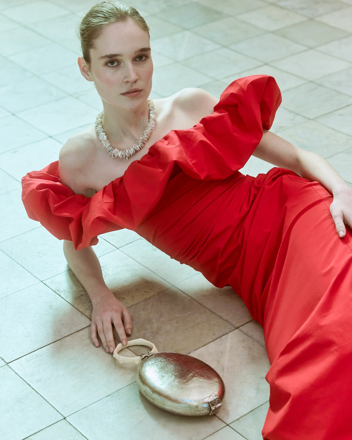 Model wearing a red dress holding The Hold silver metal handbag, handcrafted event bag with a resin top handle.