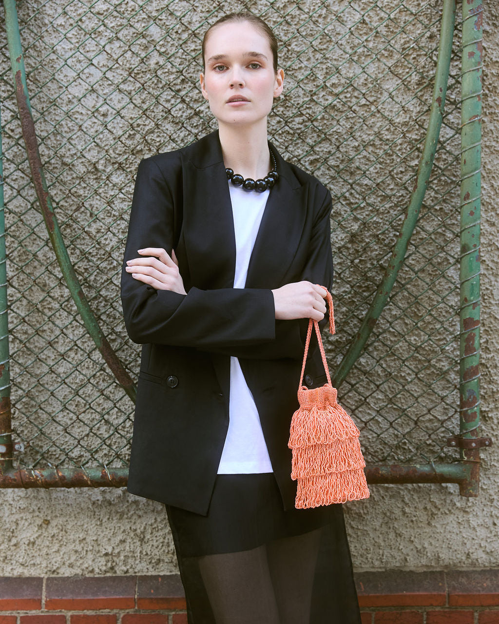 girl holding a coral beaded bag featuring three layers of beaded tassel fringe, a gathered drawstring top and long braided strap with beaded tassel ends.