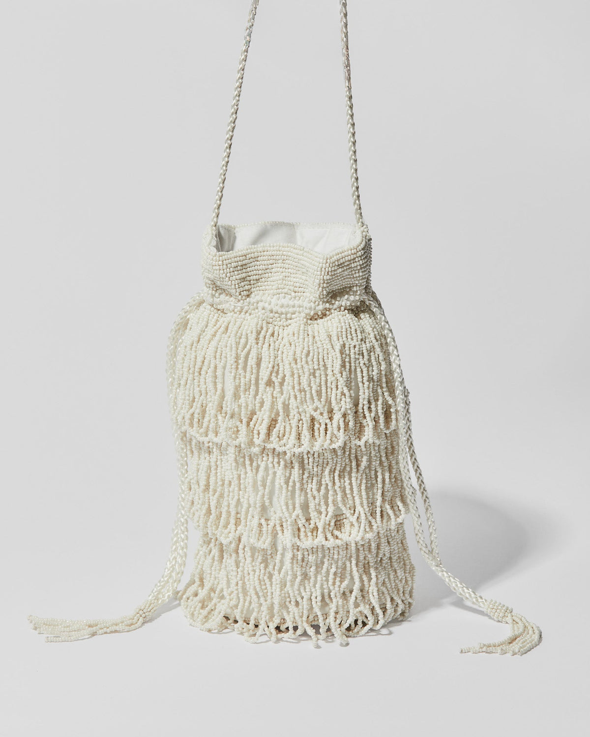 Ivory beaded fringe crossbody bag with three layered tassel tiers, gathered drawstring top and braided shoulder strap.