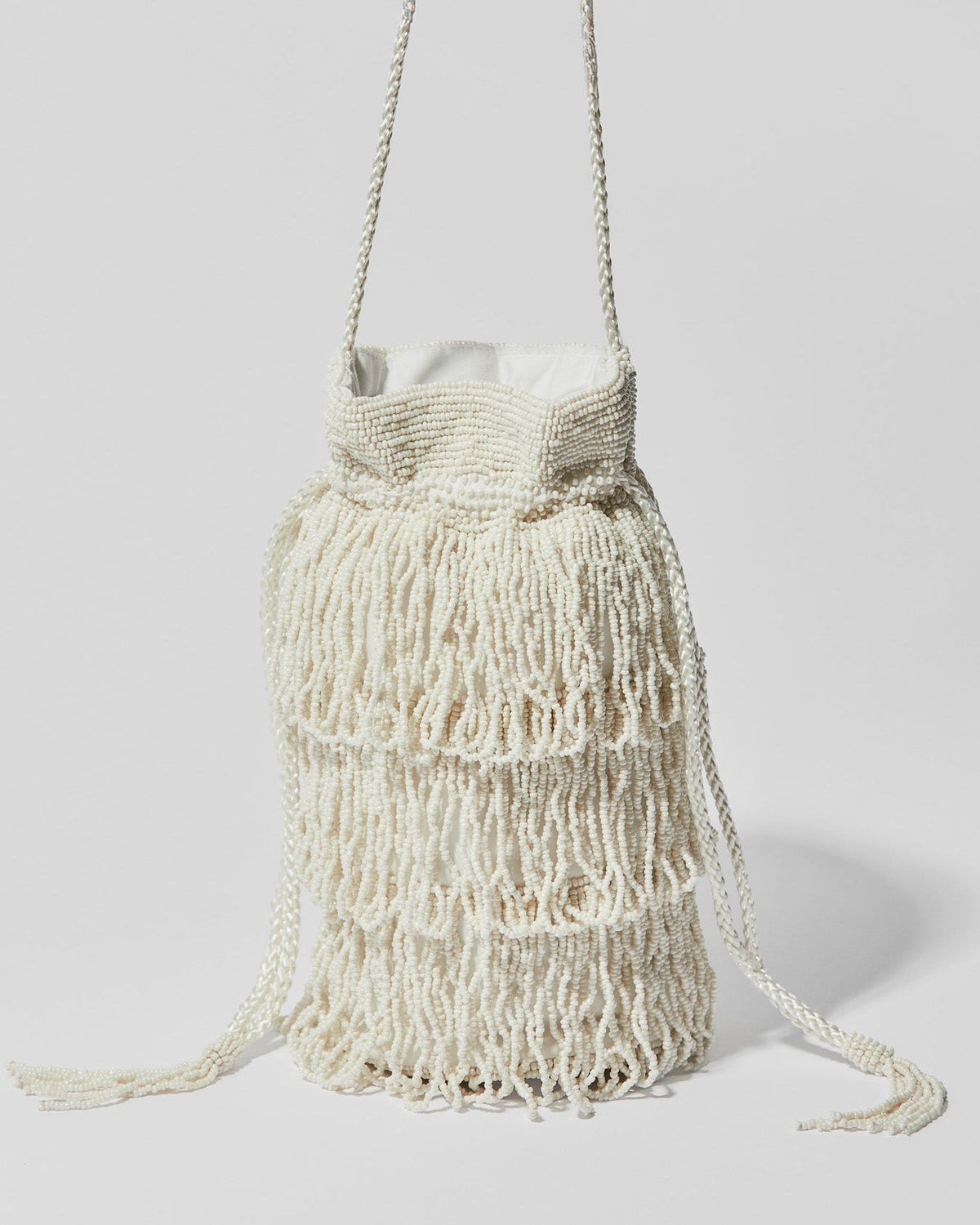 Ivory beaded fringe crossbody bag with three layered tassel tiers, gathered drawstring top and braided shoulder strap.