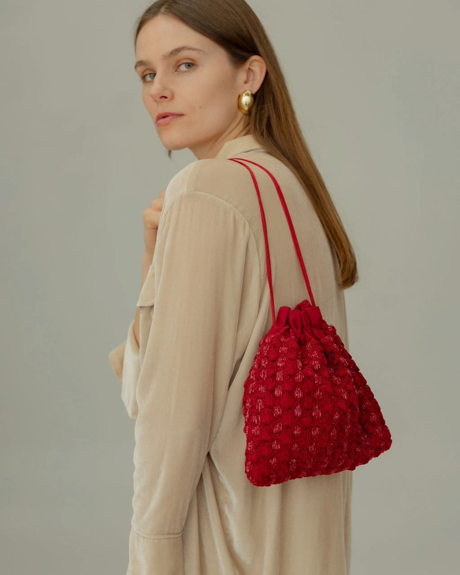 Back view of a model in a beige linen shirt carrying the red beaded pouch, showing its scale and 24cm height.