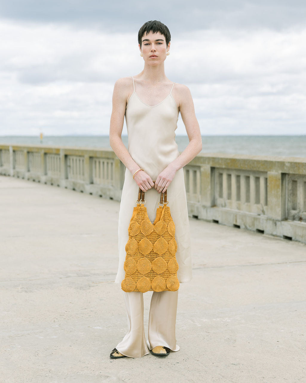 Model in a cream slip dress carrying the large ochre Enveloped Tote, demonstrating its generous volume and 42cm height.