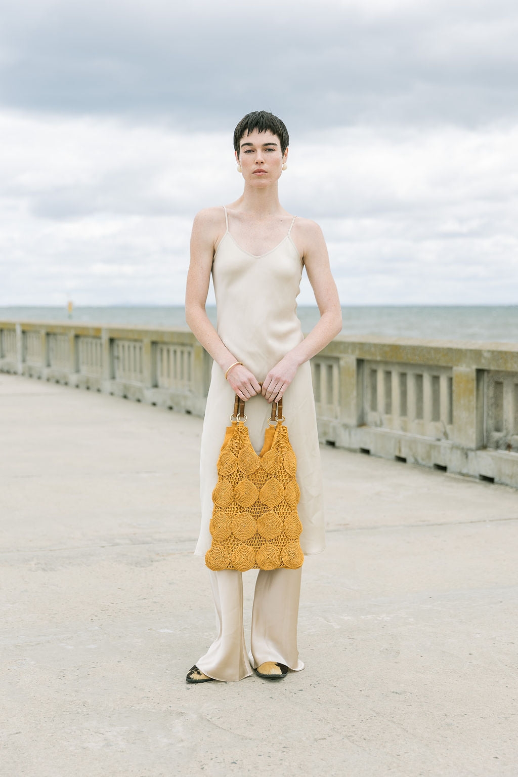 Model in a cream slip dress carrying the large ochre Enveloped Tote, demonstrating its generous volume and 42cm height.