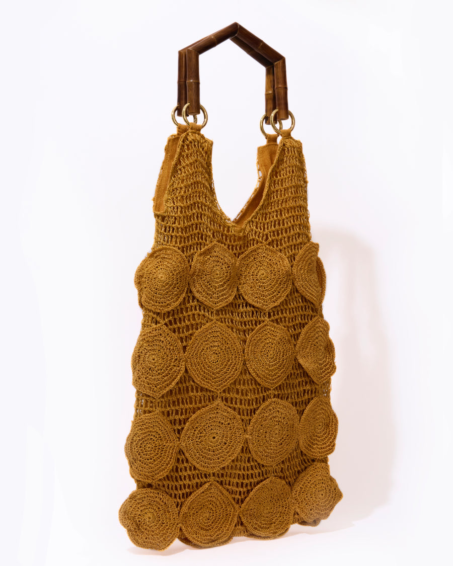 A straight-on studio view of the Enveloped Tote in ochre, highlighting the repetitive circular crochet pattern and artisanal skill.