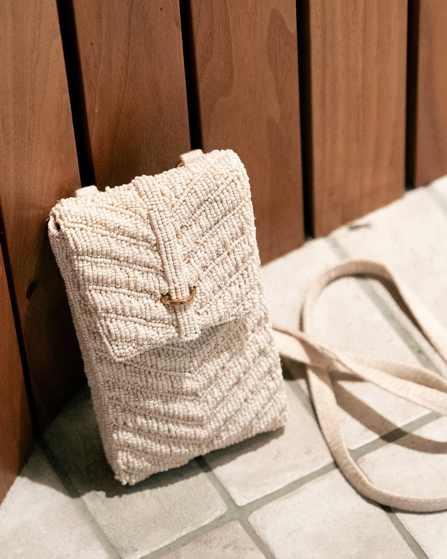 Candid shot of the white beaded mini bag resting against a wooden background, highlighting the natural jute materials and organic aesthetic.