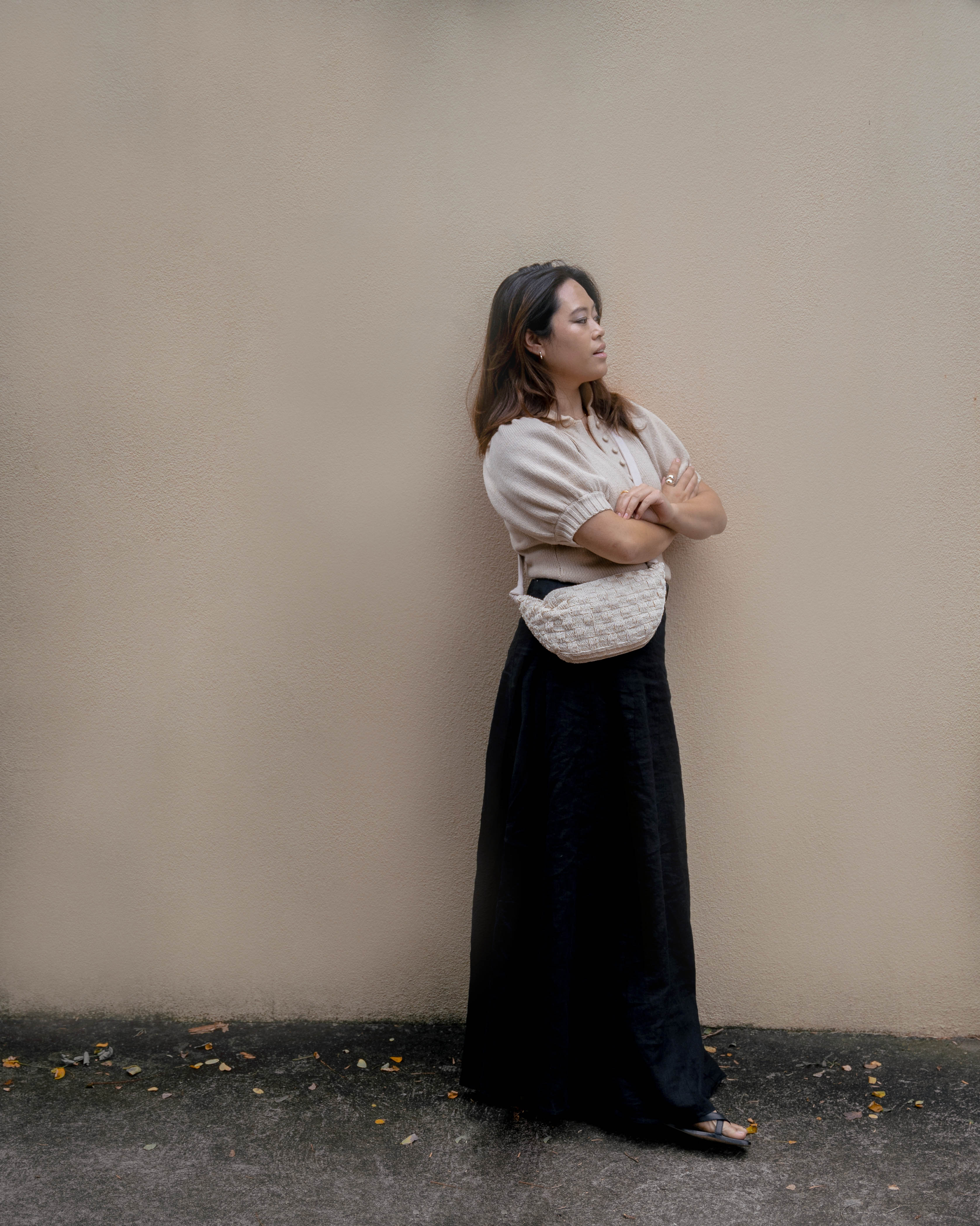 Full-length view of a customer styling the cream Moving Through bag with a neutral blouse and dark skirt for a minimalist everyday look.