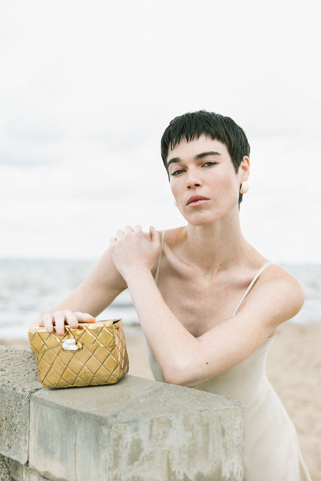 Close-up of a model holding the gold Our Longing bag, emphasising the unique character and craftsmanship of the hand-beaten brass.