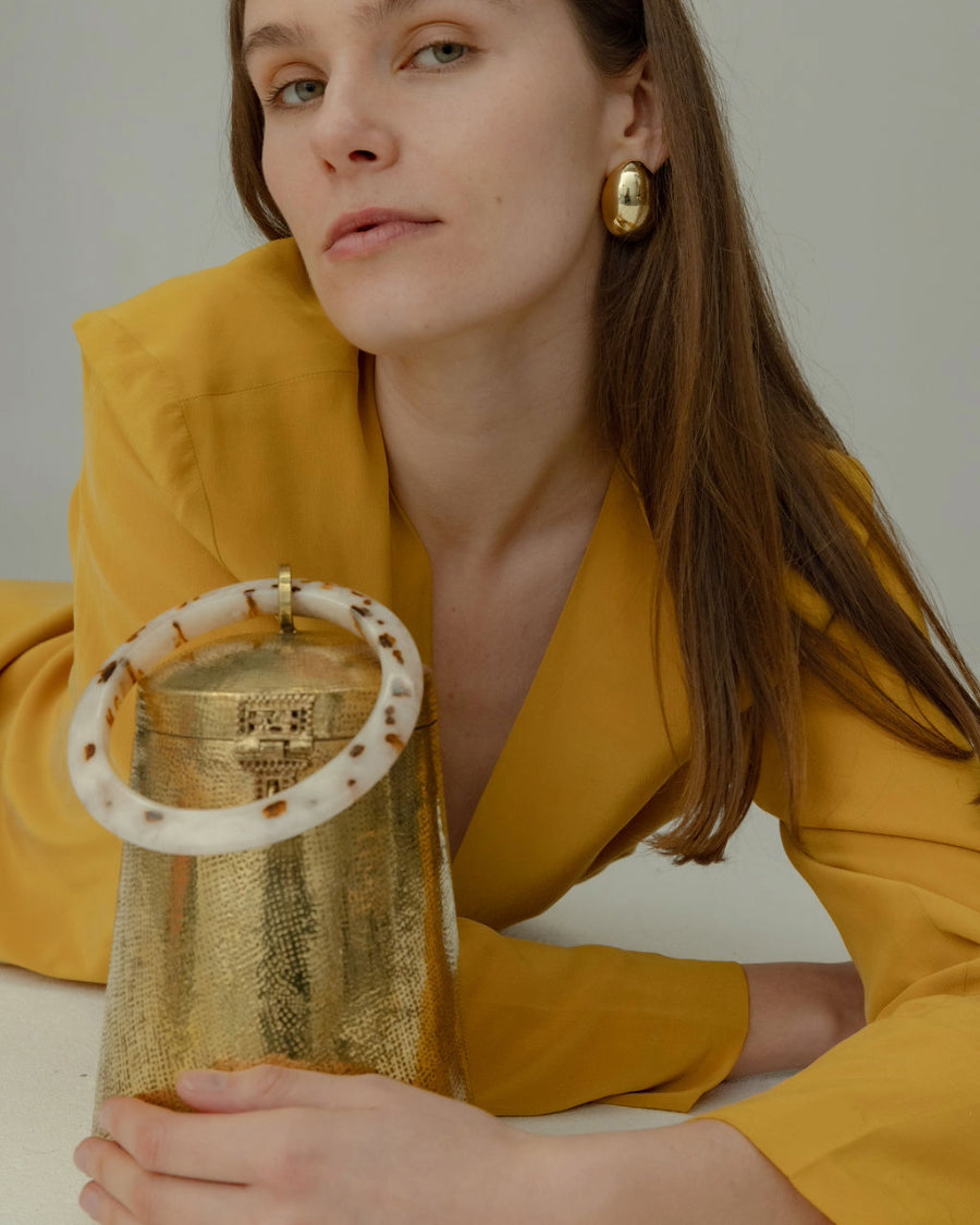 Model in a yellow blazer holding the Perception of Time gold bag by its resin handle, highlighting its unique hand-crafted character.