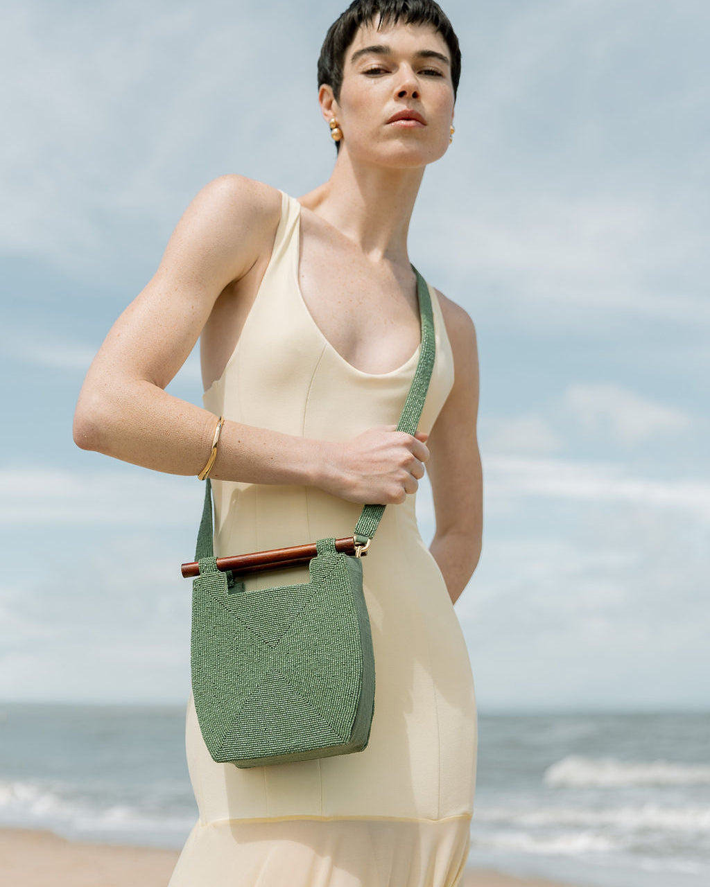 Model in a cream gown wearing the jade green Reach for Words beaded bag as a crossbody, highlighting its vibrant hand-dyed glass beads.