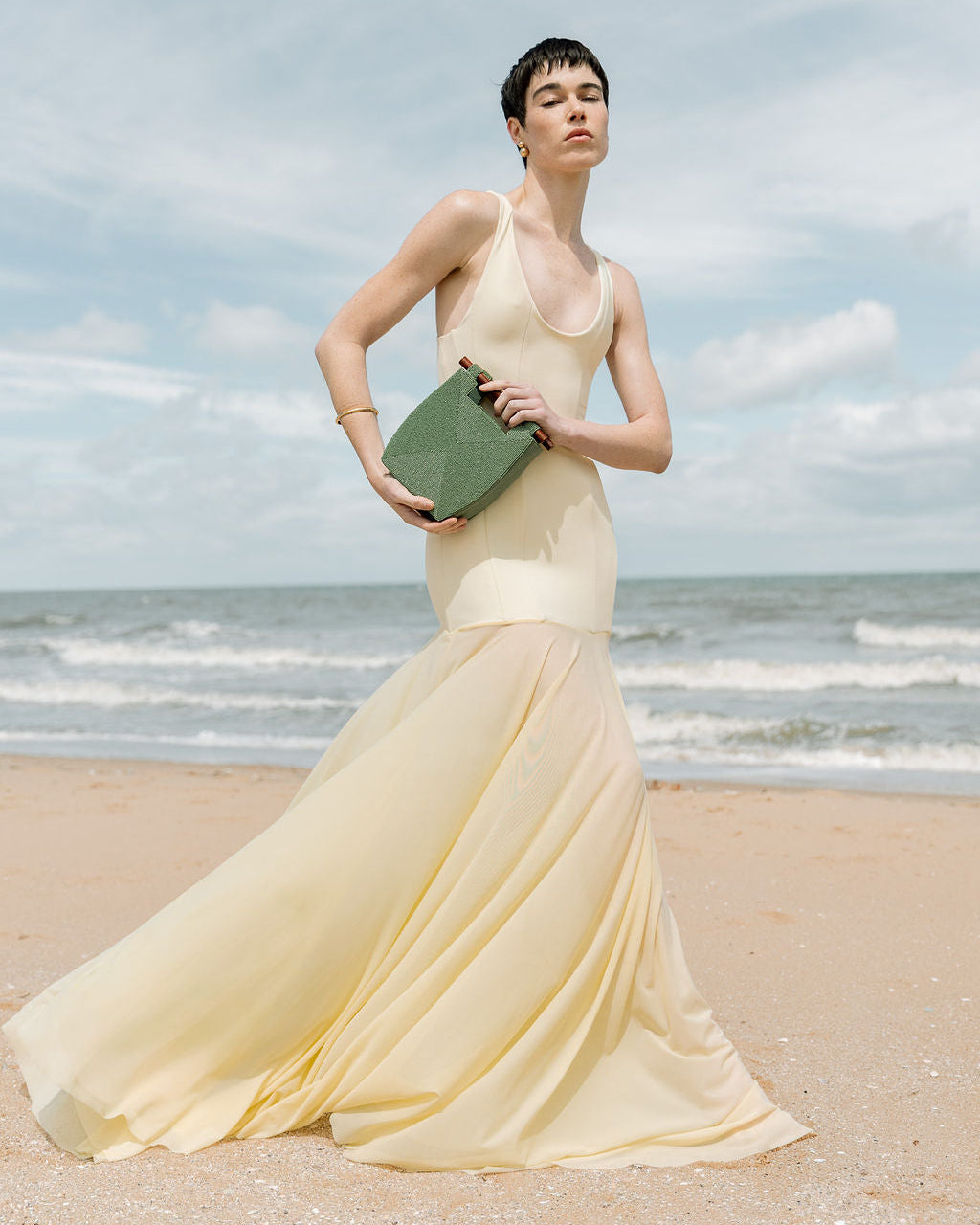 Full-length lifestyle shot of a model at the beach carrying the jade green beaded bag, showcasing its elegant scale and sculptural form.