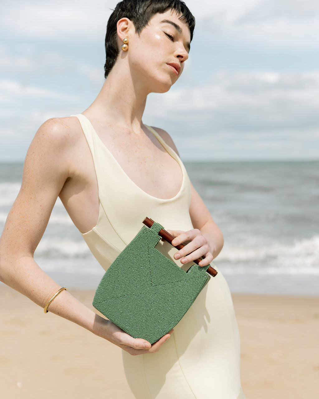 Close-up of a model holding the jade green beaded bag by its wooden bar handles, demonstrating its use as a statement top-handle bag or cross-shoulder bag.