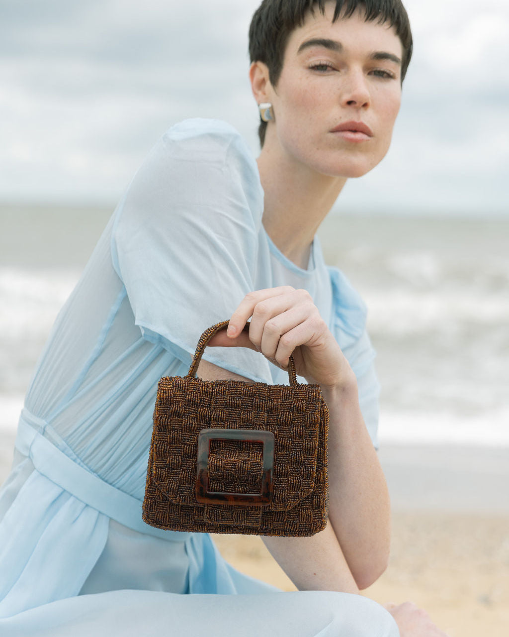 Model holding the brown beaded handbag by its top handle, demonstrating its transition from a day bag to a sculptural evening piece.