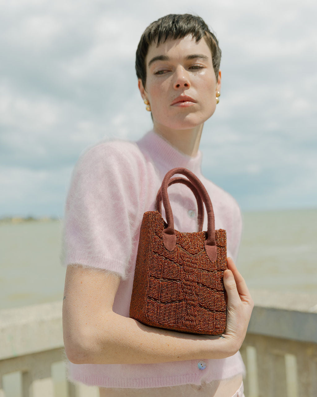Model in a pink top holding the hand-beaded burgundy bag, an artisan-made burgundy beaded bag.