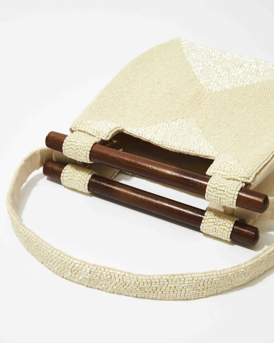 High-angle view of the white hand-beaded bag highlighting the contrast between the glass beads and the dark wooden bar handles.