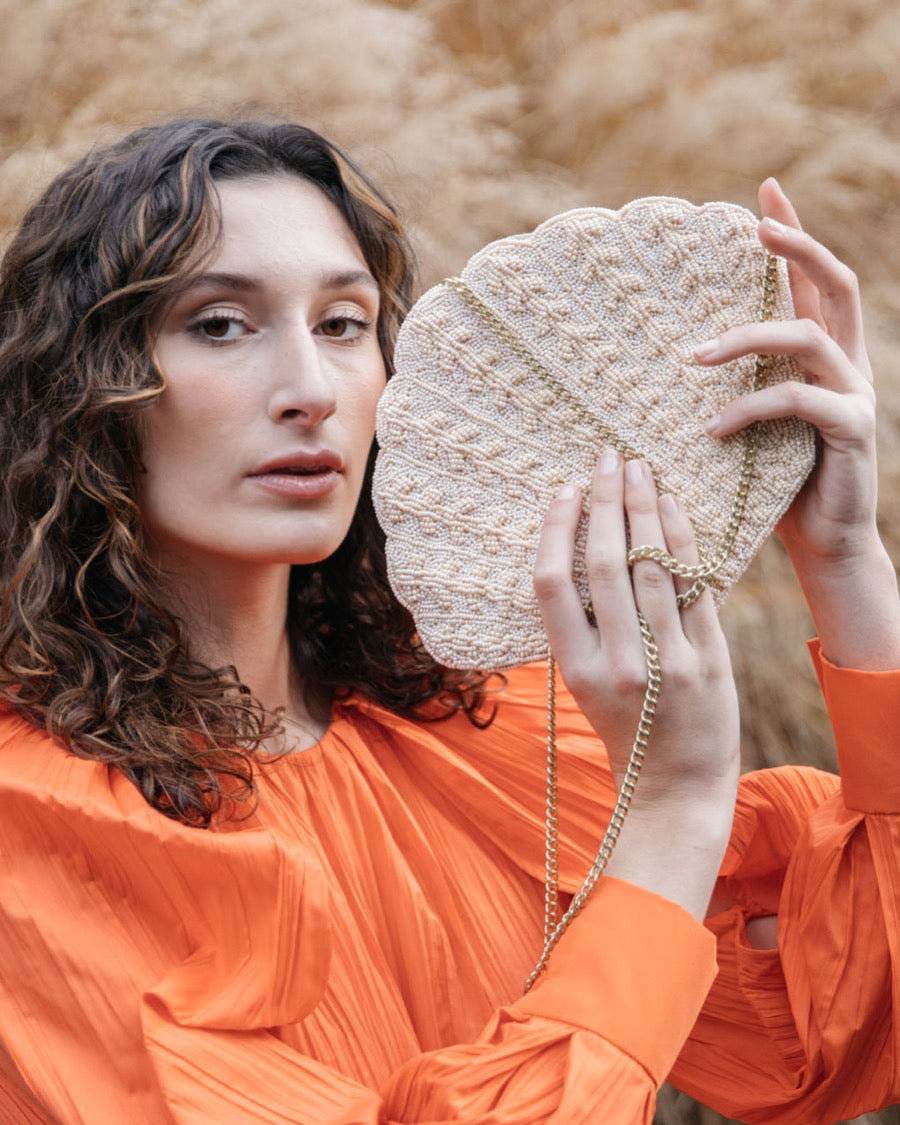 Model in a vibrant orange top holding the Stand Still beaded clutch, showcasing the sculptural elegance and hand-applied beadwork.