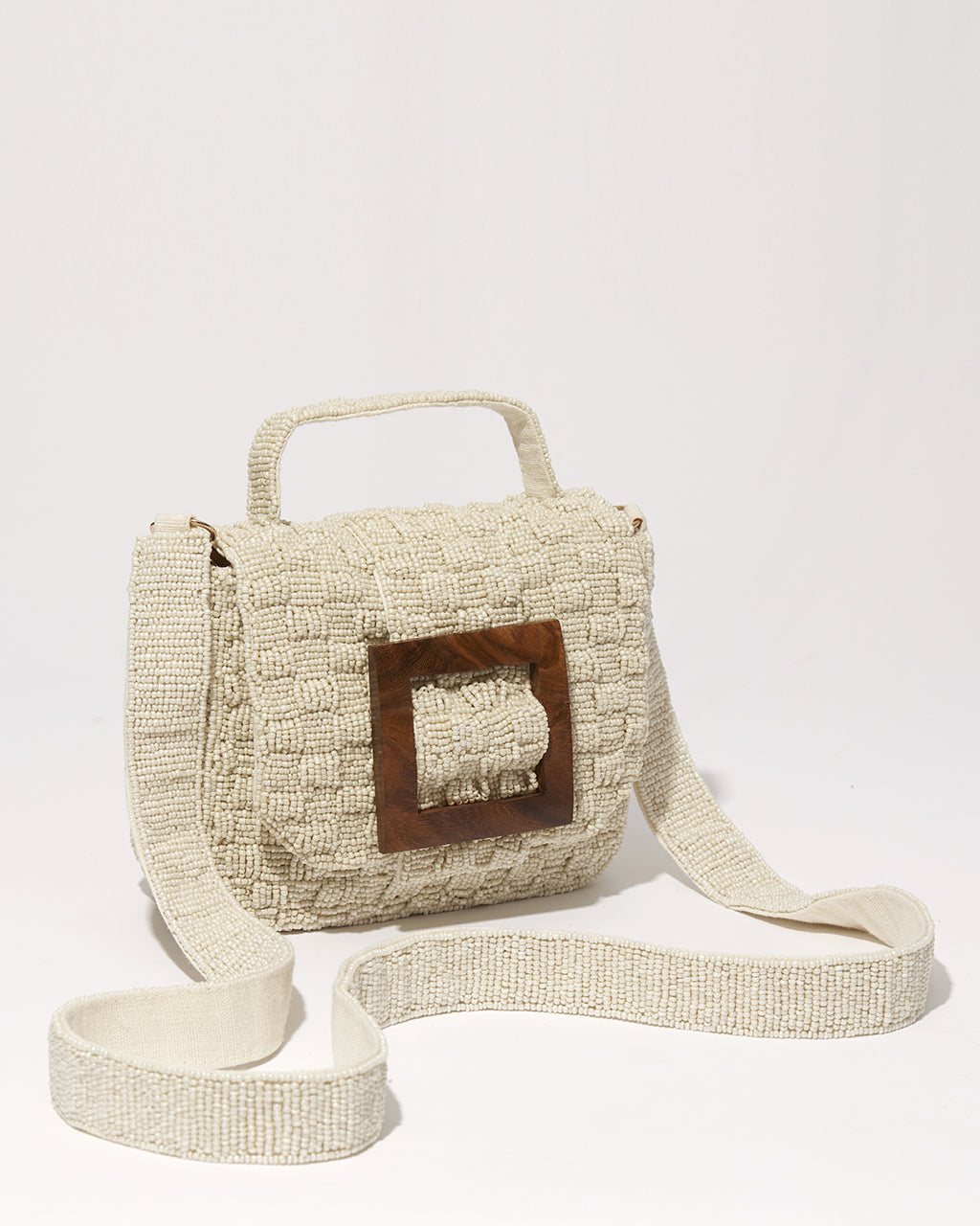 Three-quarter studio view of the white Uncovered Layers beaded bag, featuring a hand-woven sculptural design and a natural wooden buckle.