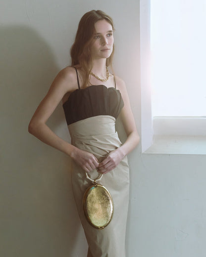 Model standing my window holding a gold metallic oval top handle handbag with a sculptural ivory coral handle by The Hold.