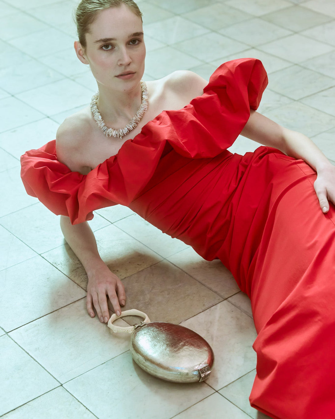 Model in red dress with silver oval shape bag with coral handle 