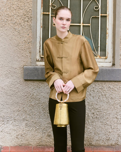 Girl in silk top holding gold shaped bell metal bag with round top handle 