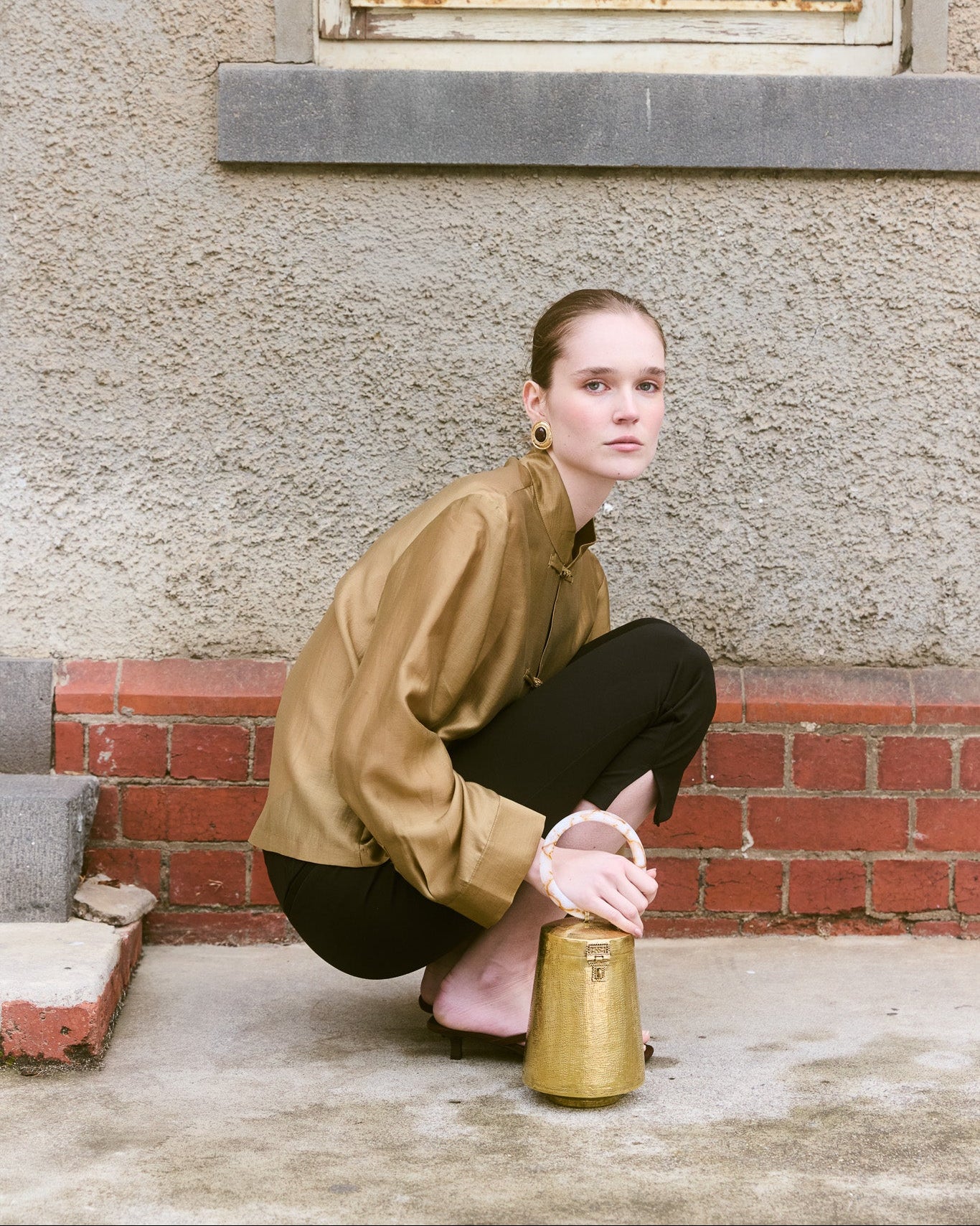 Girl kneeling holding Gold bell shape metal bag with round top handle 
