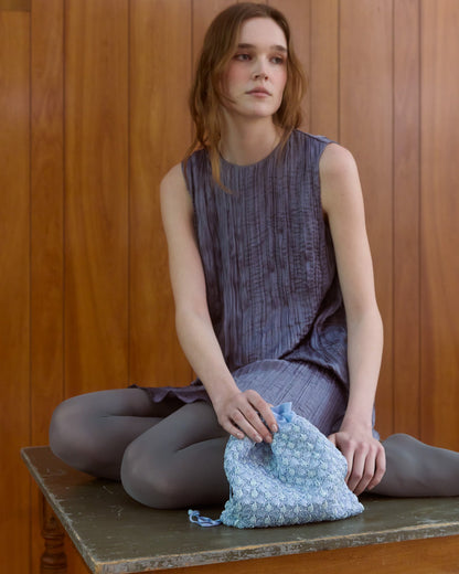 Girl wearing purple dress holding blue beaded pouch bag by the hold
