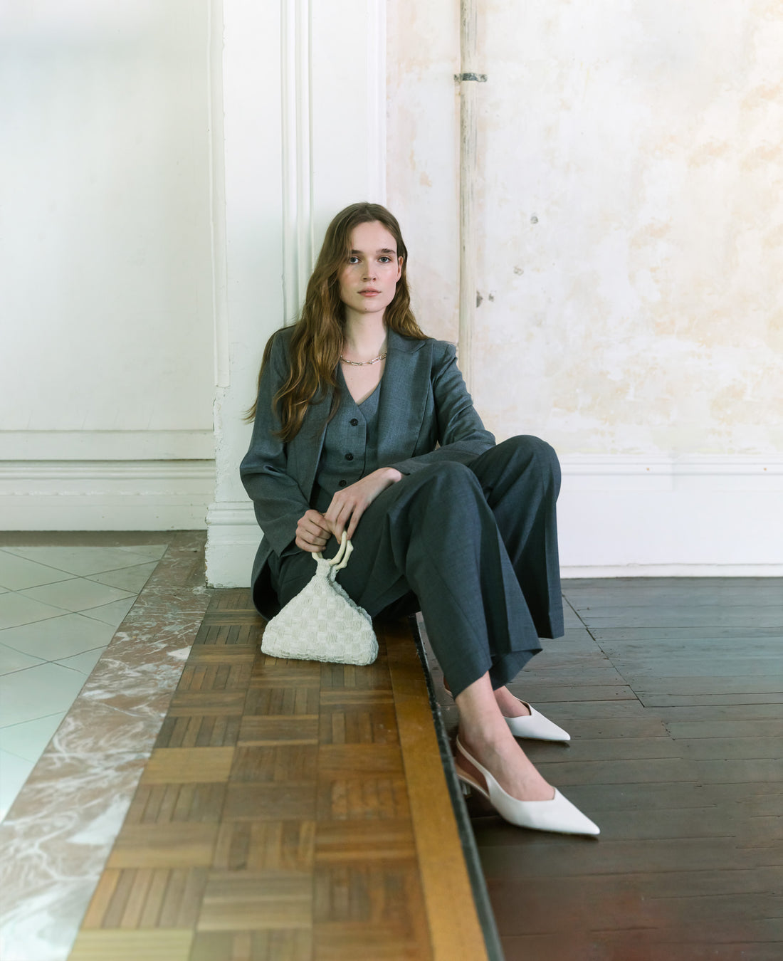 Model wearing charcoal tailoring holding an ivory beaded handbag with sculptural handle by The Hold.