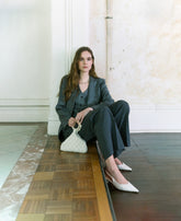 Model wearing charcoal tailoring holding an ivory beaded handbag with sculptural handle by The Hold.