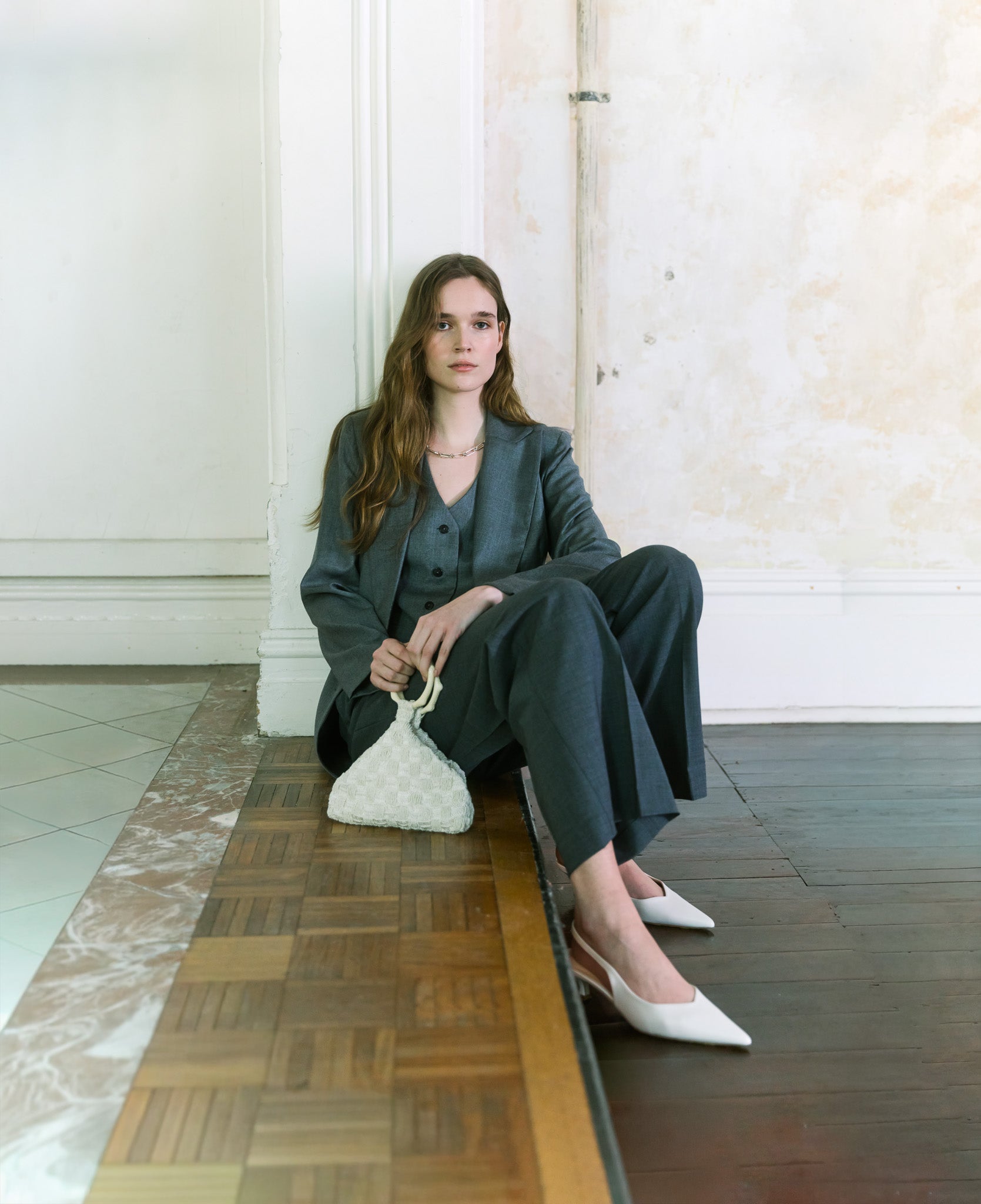 Model wearing charcoal tailoring holding an ivory beaded handbag with sculptural handle by The Hold.