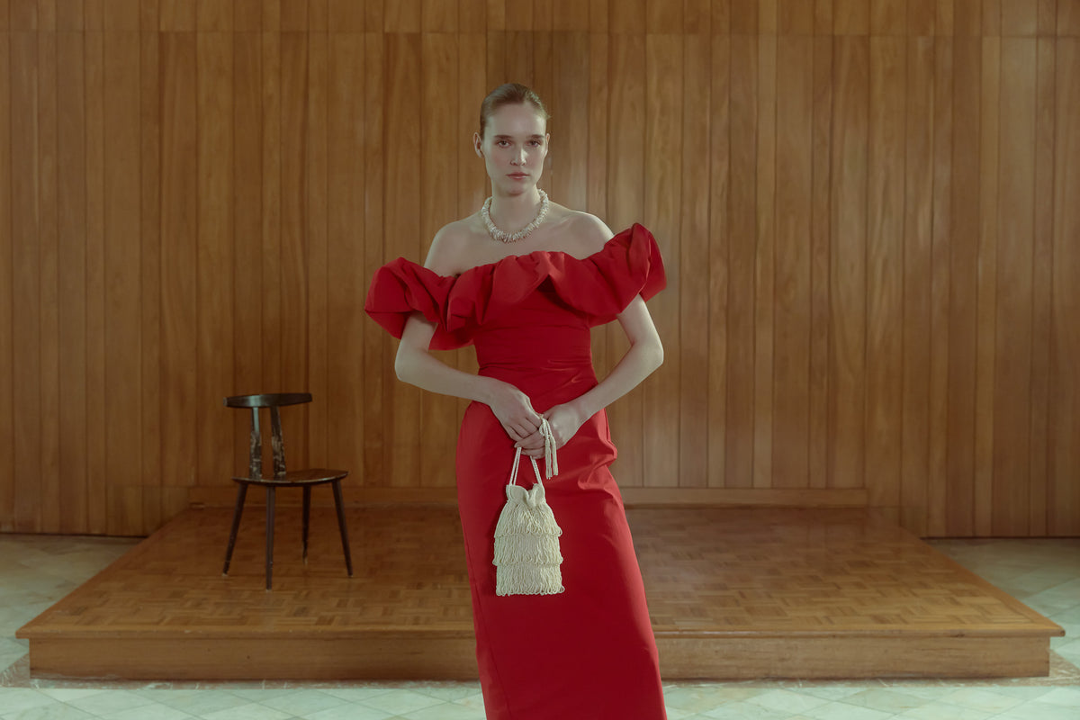 Model wearing a red dress holding The Hold ivory tassel bag, a handcrafted drawstring occasion bag with layered fringe.