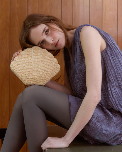 Ivory beaded shell-shaped clutch handbag by The Hold, styled with a purple dress.