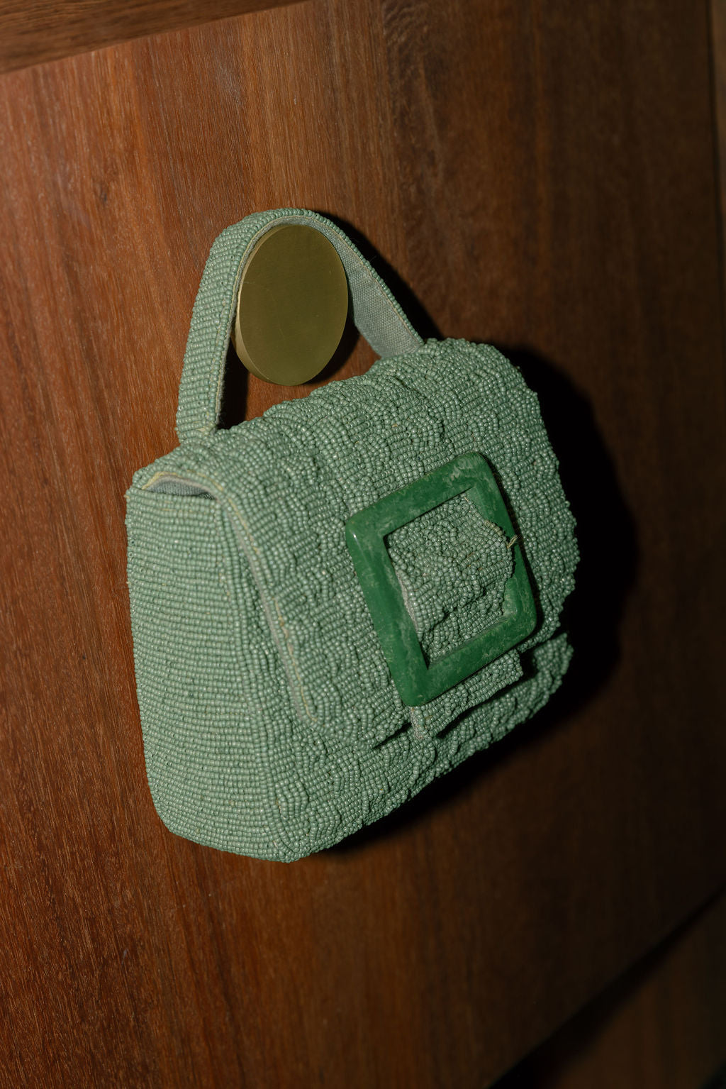 Green woven beaded handbag with top handle hanging on a wooden surface