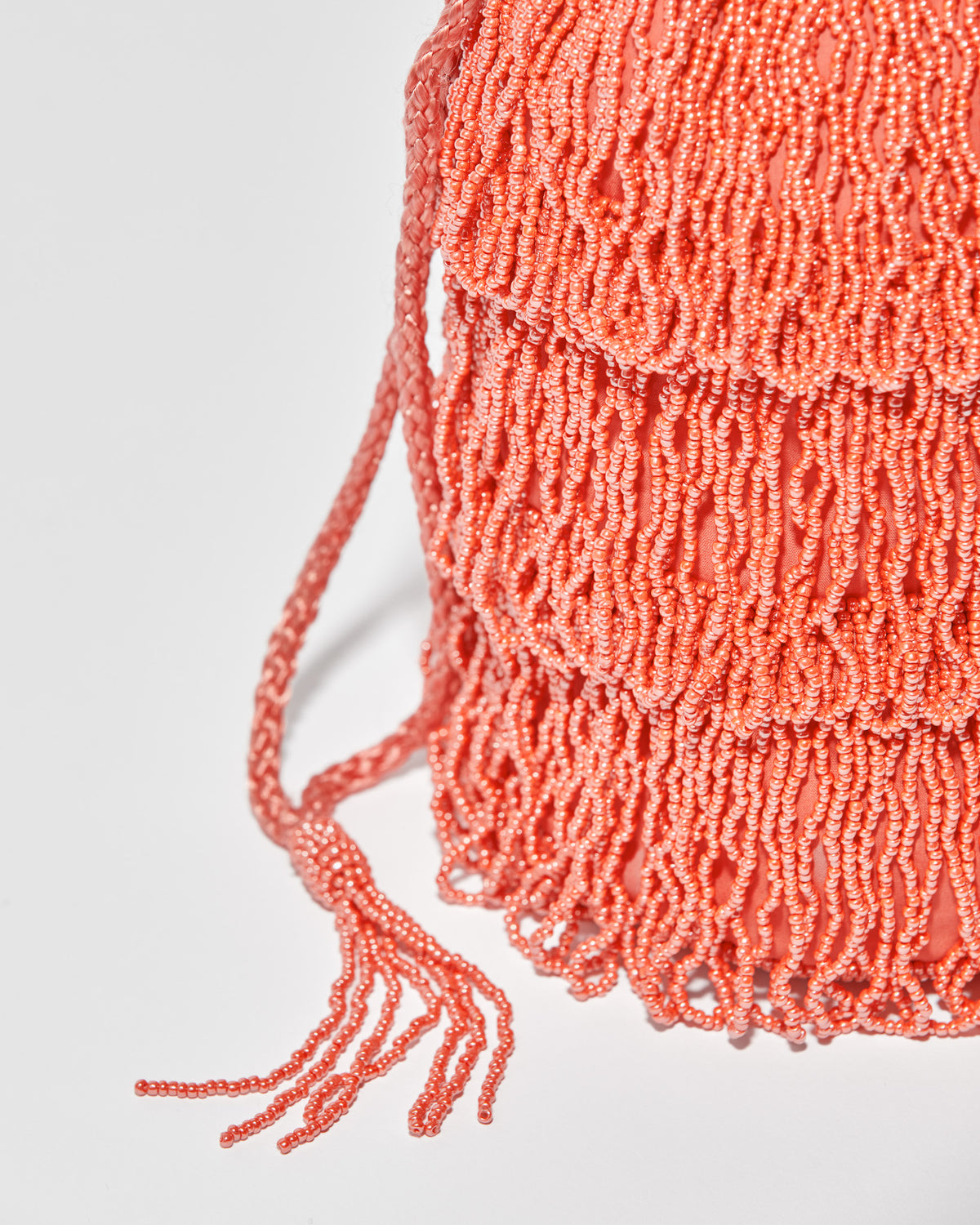side detail  and close up of beaded drawstring tassels of coral beaded bag featuring three layers of beaded tassel fringe.