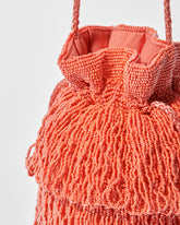 close up of detail of coral beaded bag showing beaded tassel fringe, a gathered drawstring top and long braided strap by the hold