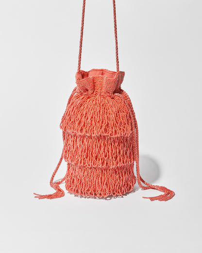 A coral beaded crossbody bag featuring three layers of beaded tassel fringe, a gathered drawstring top and long braided strap with beaded tassel ends.