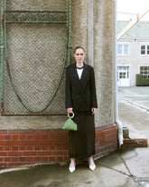 Girl standing in black suit holding a green beaded top handle bag by the hold 
