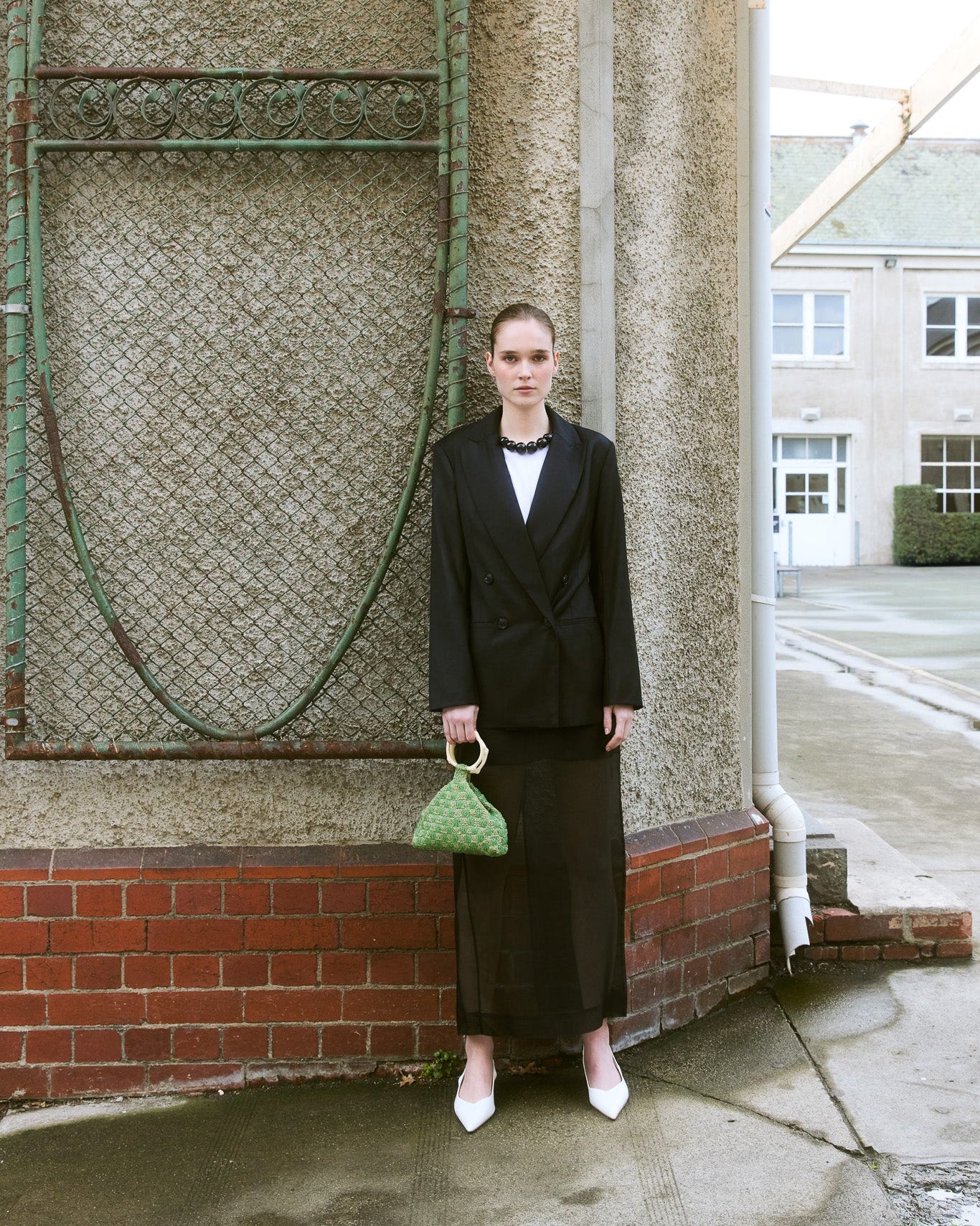 Girl standing in black suit holding a green beaded top handle bag by the hold 
