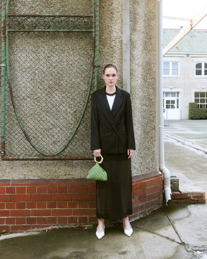 Girl standing in black suit holding a green beaded top handle bag by the hold 
