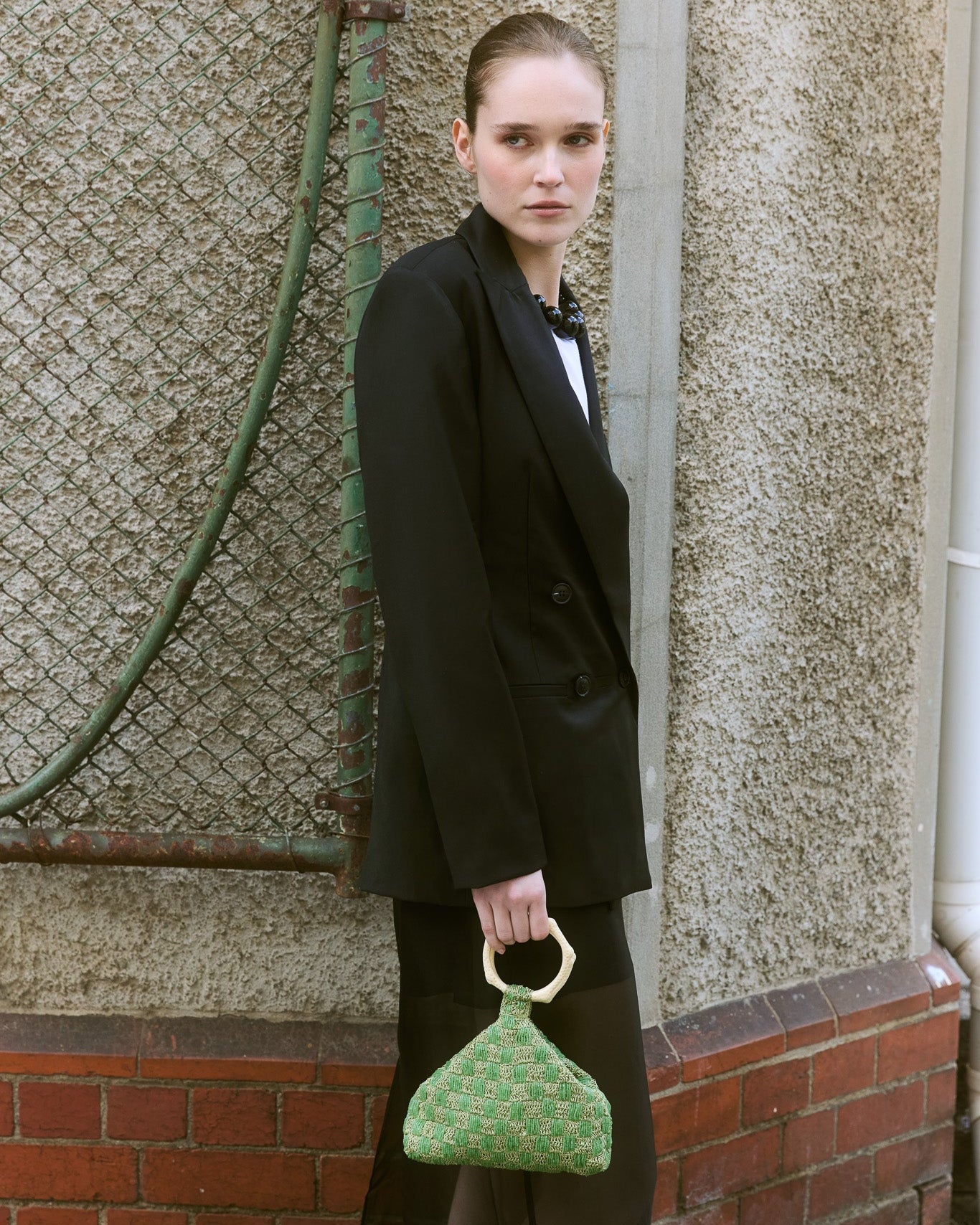 Model in black Blazer holding a green beaded bag with coral handle 