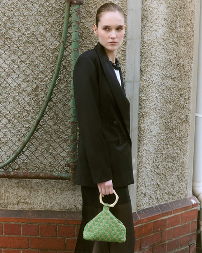 Model in black Blazer holding a green beaded bag with coral handle 
