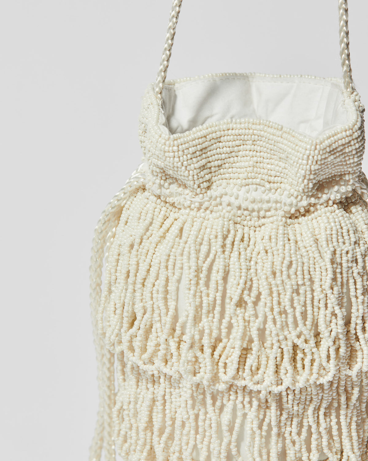 close up Ivory beaded fringe crossbody bag with three layered tassel tiers, gathered drawstring top and braided shoulder strap.