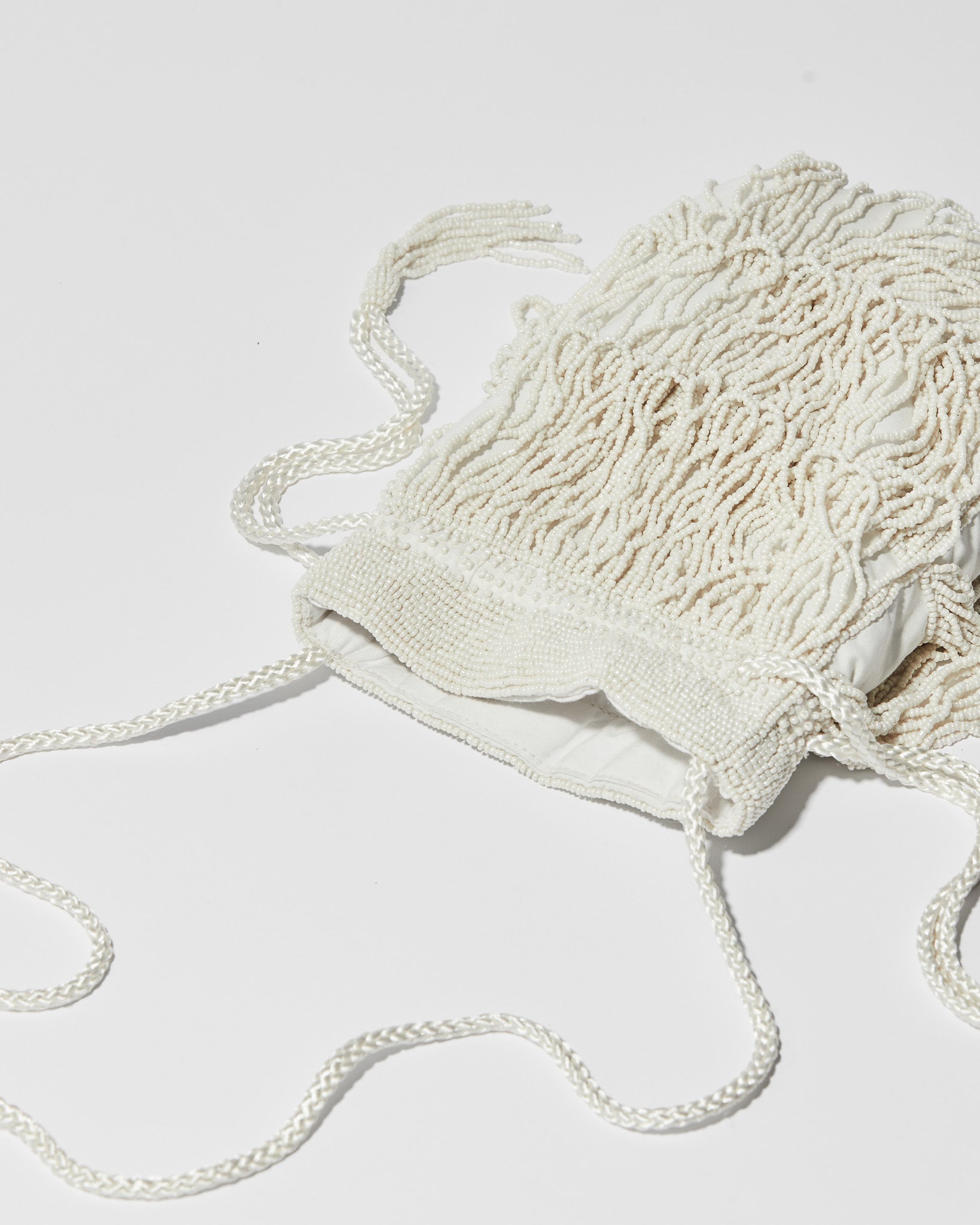 Lying flat Ivory beaded fringe crossbody bag with three layered tassel tiers, gathered drawstring top and braided shoulder strap.