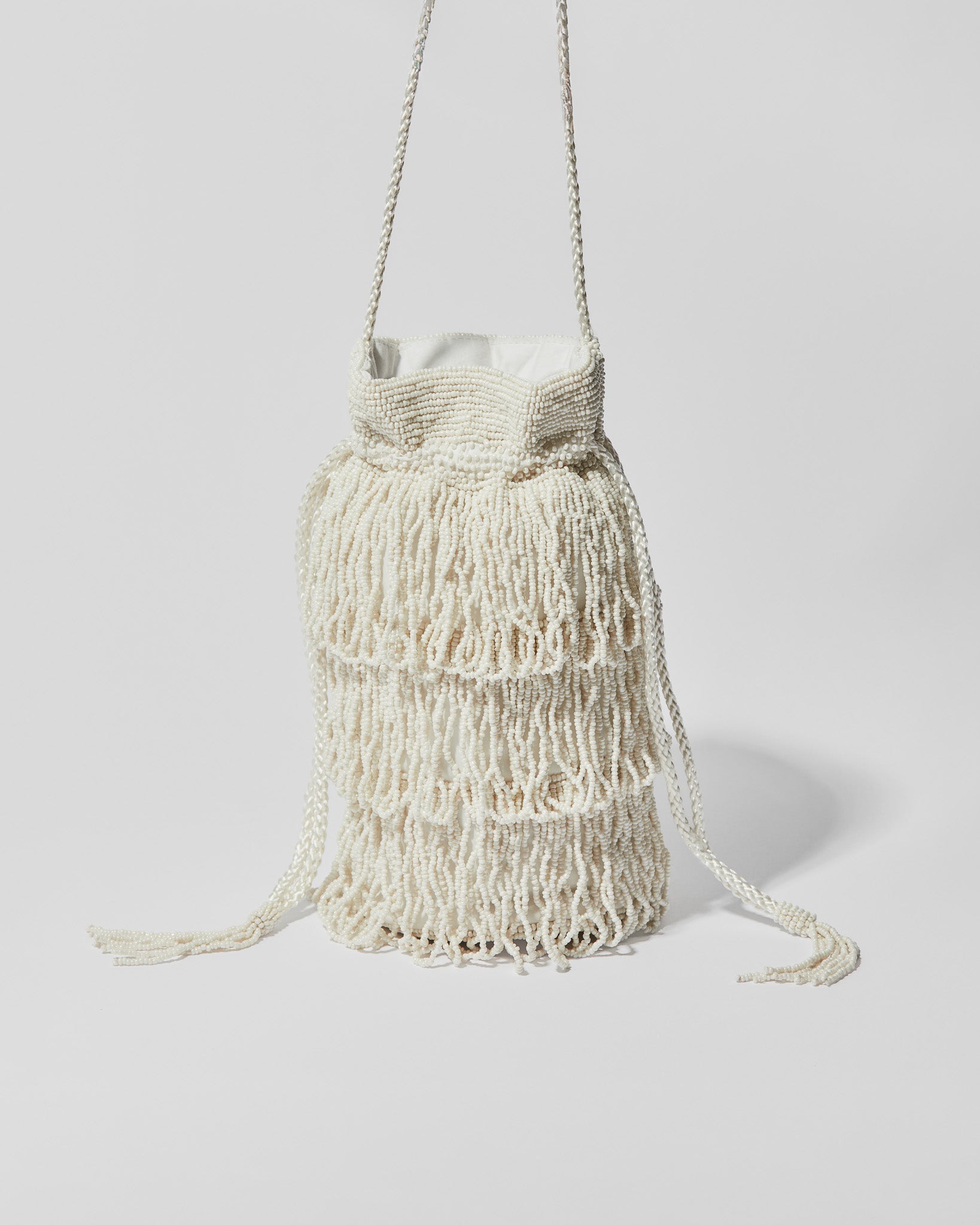 Ivory beaded fringe crossbody bag with three layered tassel tiers, gathered drawstring top and braided shoulder strap.