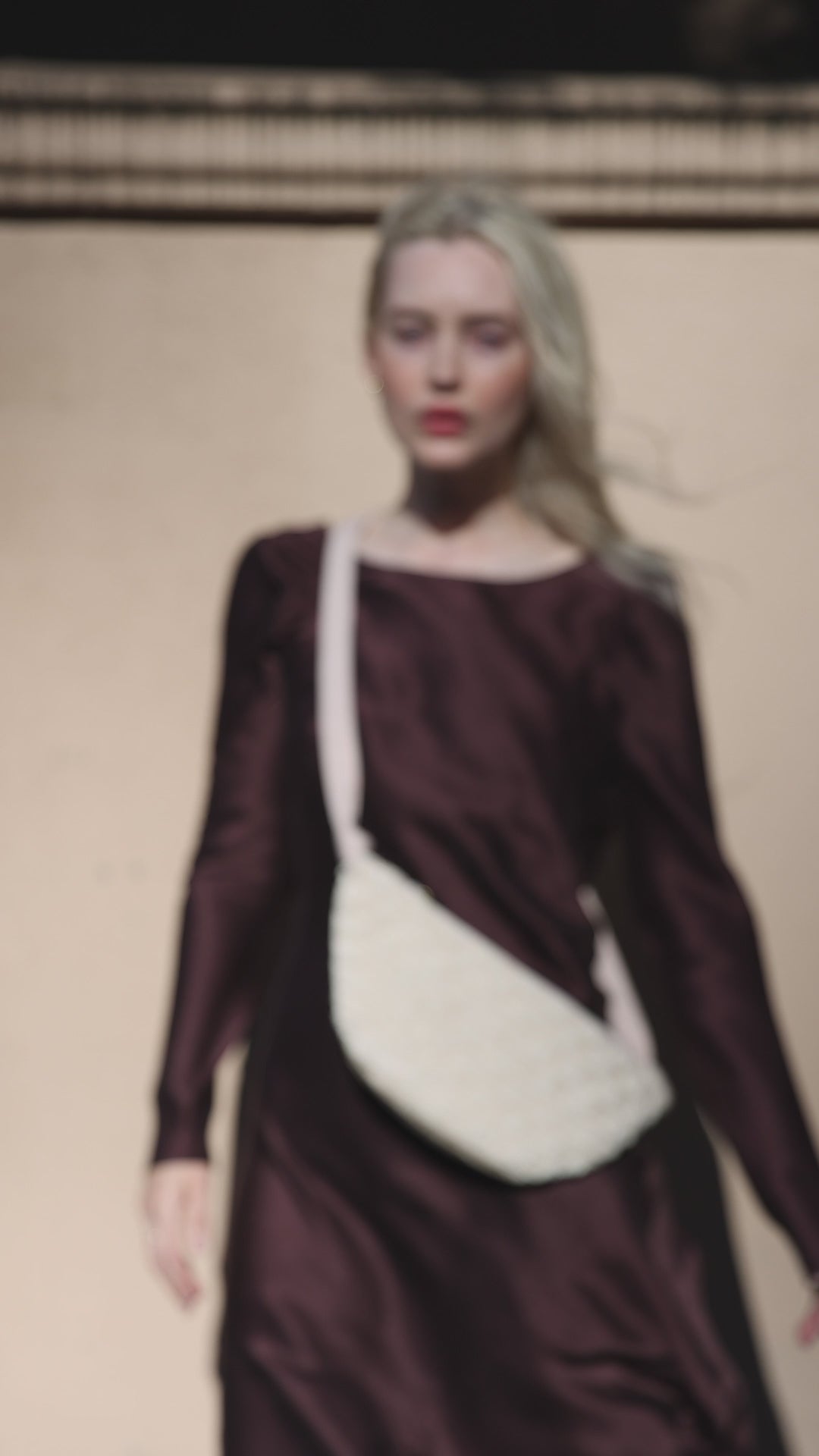 A model walking with the ivory Moving Through bag, showcasing how the sculptural piece moves comfortably with the body