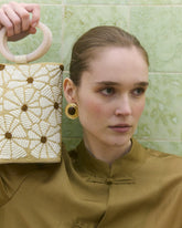 Girl in brown up holding up a floral beaded  bag with top handle 