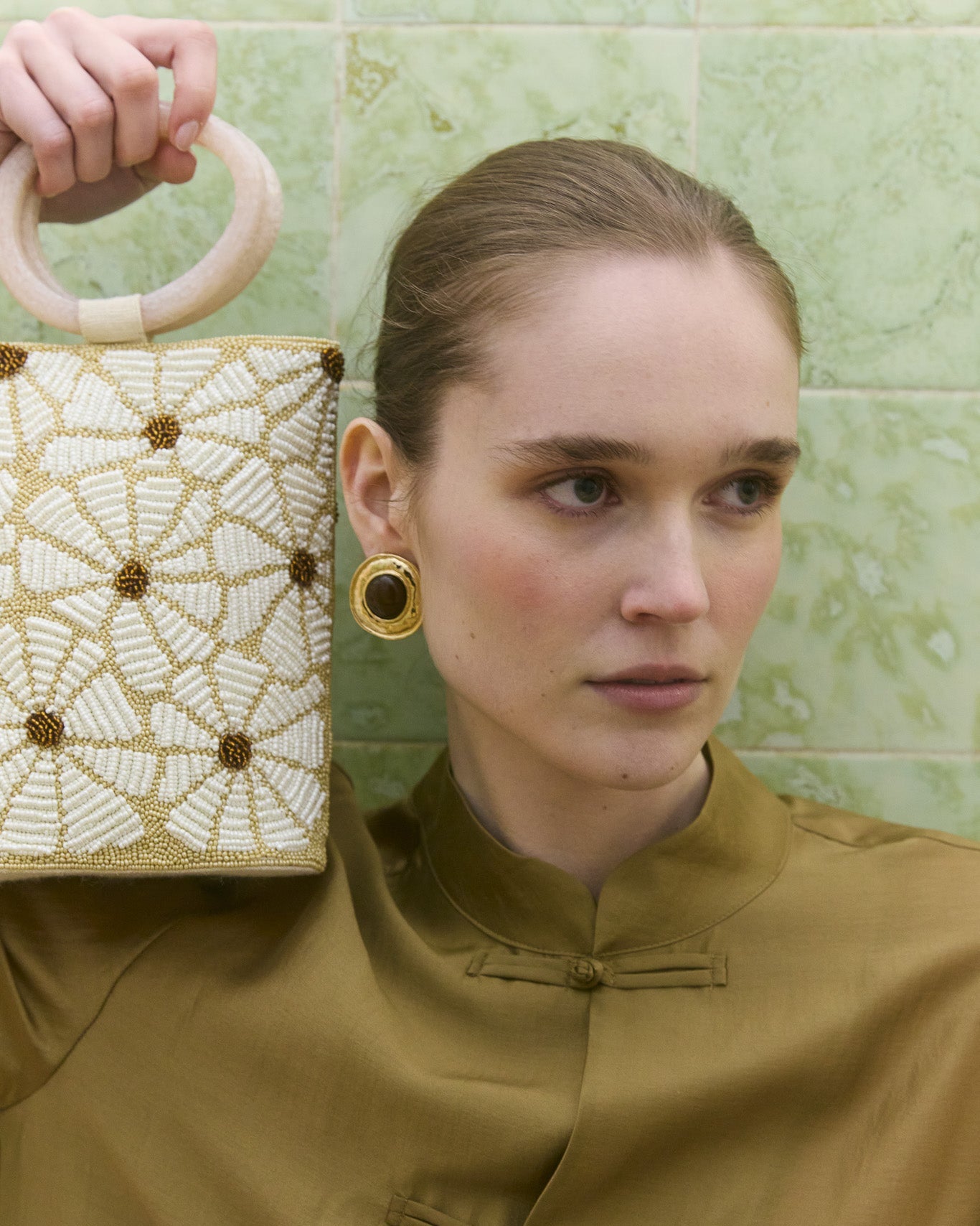 Girl in brown up holding up a floral beaded  bag with top handle 