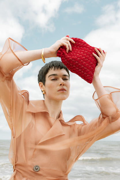 Close-up of a model holding the As Always pouch, highlighting the intricate hand-woven glass beads and vibrant red color.