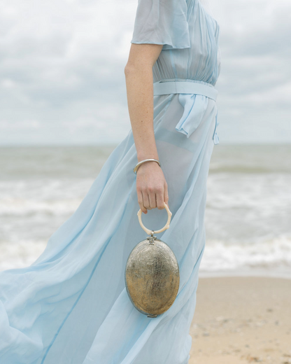 front view of a model styling the silver hand-beaten metal bag as an event accessory, highlighting its metallic surface  and top handle carry.
