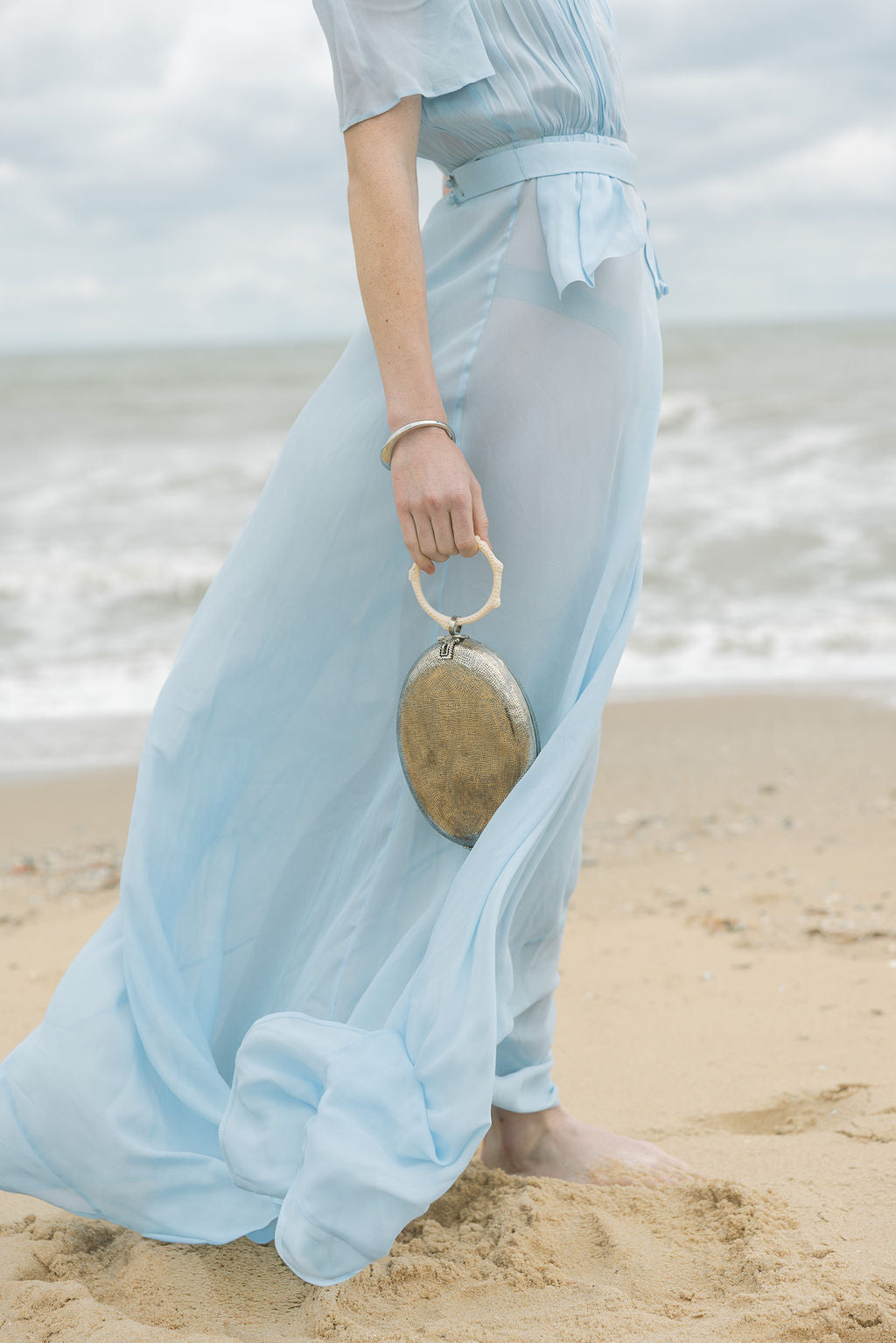 Side view of a model styling the silver hand-beaten metal bag as an event accessory, highlighting its thin 4cm depth and ergonomic carry.