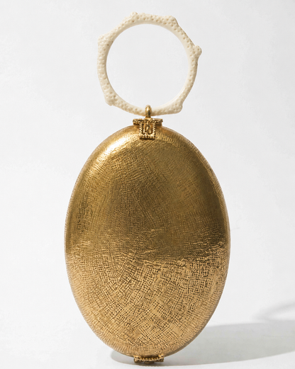 Front studio view of the Capacity for Presence Gold metal bag, featuring an oval hand-beaten brass body and a cream coral-inspired resin handle.